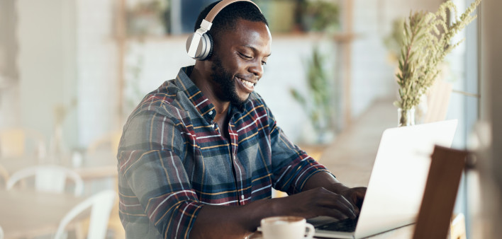 Cropped shot of a handsome young businessman wearing headphones to listen to music and using his computer in a cafe