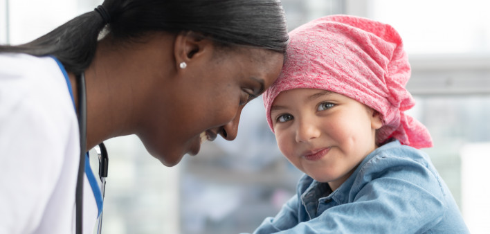 A cute elementary age girl with cancer is wearing a pink scarf on her head.