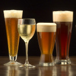 An assortment of glasses of wine and beer including a classic pilsner flute, a sparkling wine glass, an American half pint glass, a weizen or wheat beer glass, an American pint glass, a white wine glass, and a red wine glass.