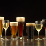 An assortment of glasses of wine and beer including a classic pilsner flute, a sparkling wine glass, an American half pint glass, a weizen or wheat beer glass, an American pint glass, a white wine glass, and a red wine glass.