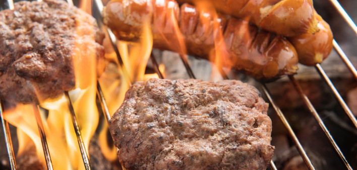 hotdogs and hamburgers on a grill with flames