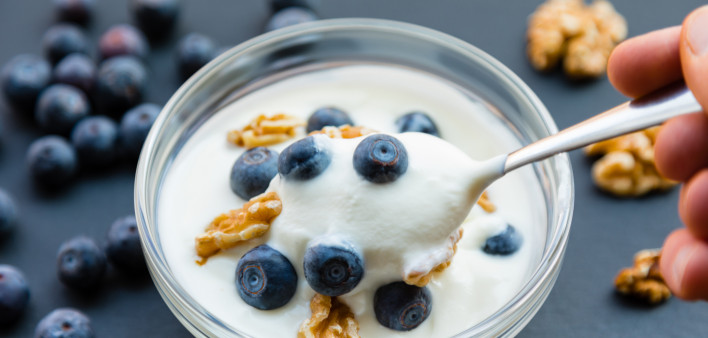 bowl of yogurt and blueberries with walnuts and a spoon