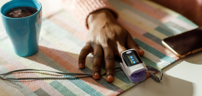 A black black woman measures her oxygen level at home using a pulse oximeter.