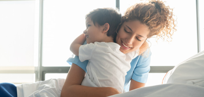 Beautiful sweet little boy hospitalized in the pediatrics ward hugging young nurse both smiling