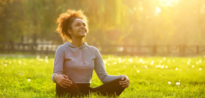Happy young woman sitting outdoors in yoga position