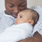 Beautiful African American mother in a hospital gown holds her newborn baby