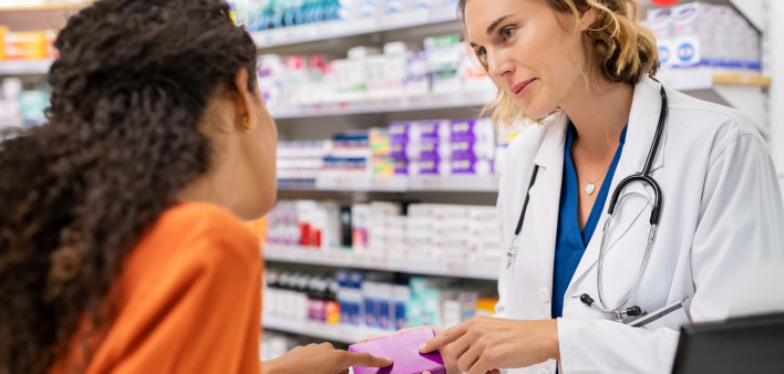 Pharmacist giving medicine box to customer in pharmacy. Doctor showing and explaining medicine dose to customer. Mature pharmacist giving advice on medicaments, while serving young african woman.