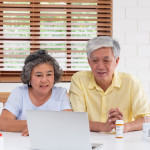 Asian couple seniors use laptop video conference with doctor about illness and prescription pill in living room at home