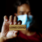 Masked Asian man show wooden sign with wording "Long Covid"