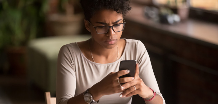 Upset confused african woman holding cellphone having problem with mobile phone,