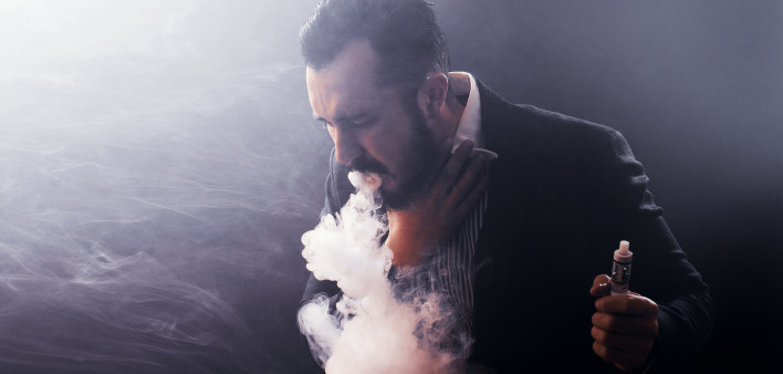 Man coughing out vaponizer holding a vape mod in his hand.