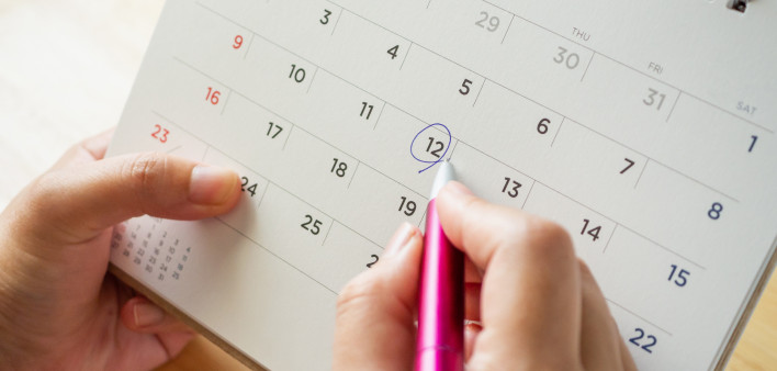 Calendar page with female hand holding pen on desk table