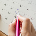 Calendar page with female hand holding pen on desk table