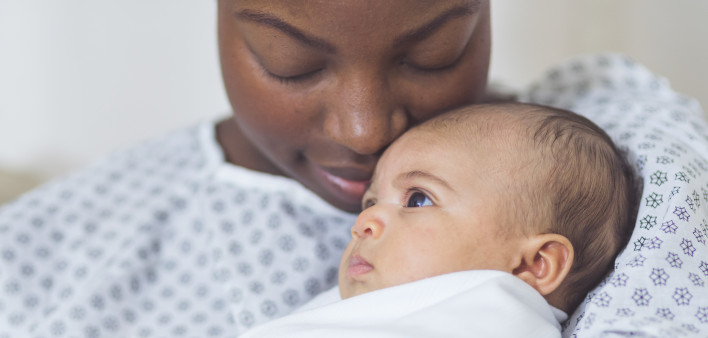 Beautiful African American mother in a hospital gown holds her newborn baby