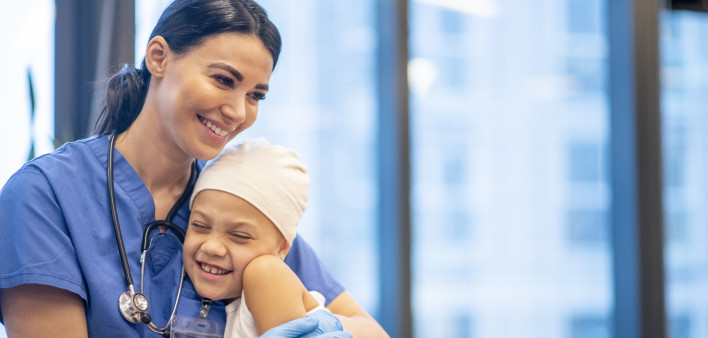 Nurse Hugging Young Cancer Patient stock photo A young Latin female nurse hugs her cancer patient as they enjoy a brief moment together. The young girl is smiling and happy. The nurse is wearing blue scrubs with a stethoscope around her neck, while the yo