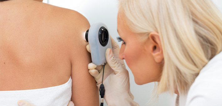 Female dermatologist examining female patient's skin with dermascope, doctor is carefully looking for signs of skin cancer