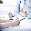 Doctor and female patient sitting at the desk and talking in clinic near window. Medicine and health care