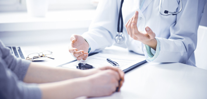 Doctor and female patient sitting at the desk and talking in clinic near window. Medicine and health care