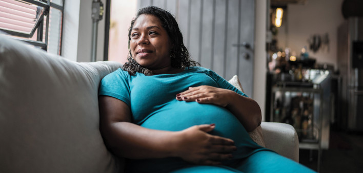 Pregnant Black woman holder her belly on couch