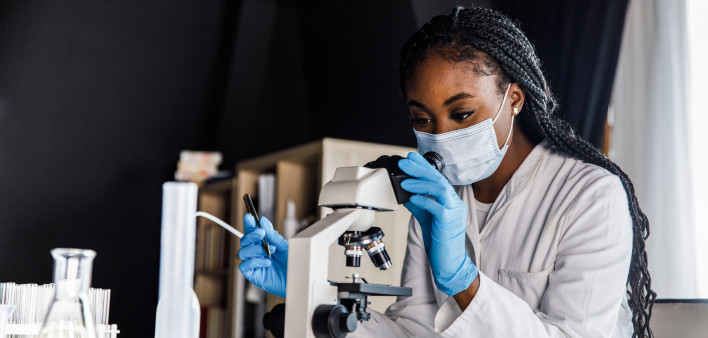 female scienitst analyzing a sample under a microscope while doing research