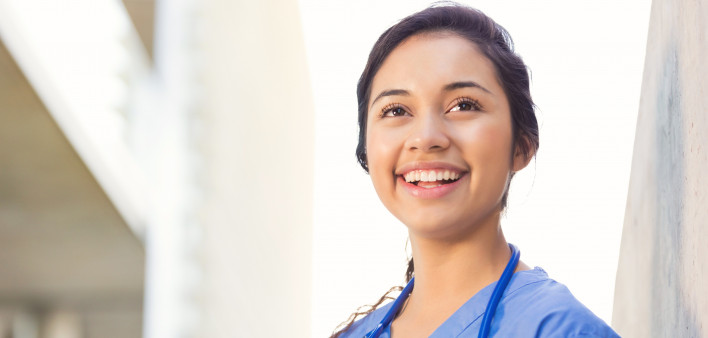Young adult Hispanic woman is smiling while standing outside on college campus.