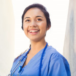 Young adult Hispanic woman is smiling while standing outside on college campus.