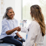 Unrecognizable doctor shakes hands with senior female patient stock photo