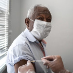 Nurse applying vaccine on patient's arm using face mask