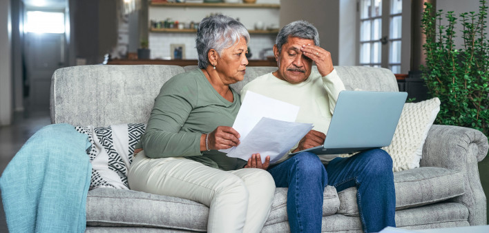 Shot of a senior couple looking stressed while using a laptop and going through paperwork on the sofa