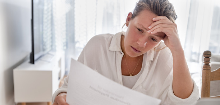 Woman looking worried holding paperwork at home. She is reading a financial bill or a letter with bad news. She looks very stressed and upset.