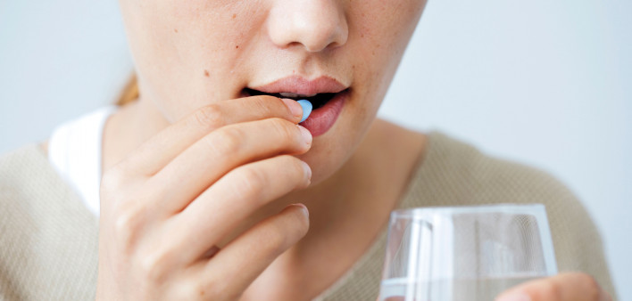 Girl taking a blue pill with glass water