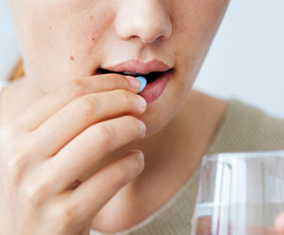 Girl taking a blue pill with glass water