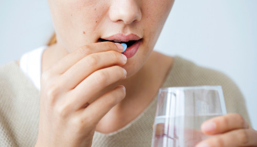 Girl taking a blue pill with glass water