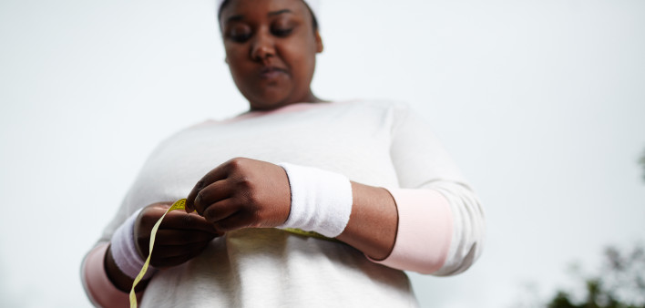Low angle view of overweight African woman measuring her waist after sports training