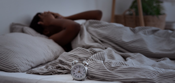 Sleepless, woman suffering from insomnia, sleep apnea or stress, headache or migraine. Tired and exhausted african american lady awake in middle of night, near alarm clock with time in dark, panorama