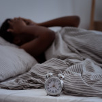 Sleepless, woman suffering from insomnia, sleep apnea or stress, headache or migraine. Tired and exhausted african american lady awake in middle of night, near alarm clock with time in dark, panorama