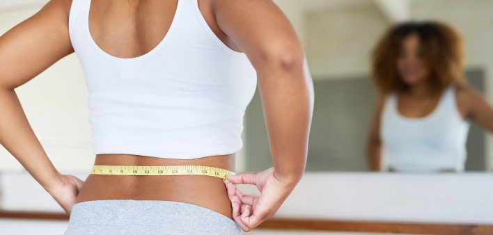 ropped shot of a young woman measuring her waist in the bathroom