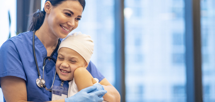 Nurse Hugging Young Cancer Patient stock photo A young Latin female nurse hugs her cancer patient as they enjoy a brief moment together. The young girl is smiling and happy. The nurse is wearing blue scrubs with a stethoscope around her neck, while the yo