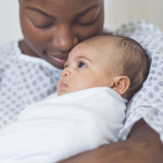 Beautiful African American mother in a hospital gown holds her newborn baby