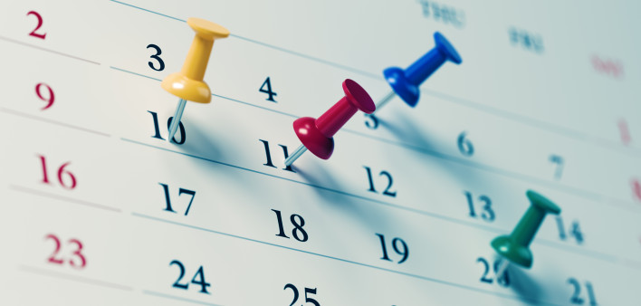 White calendar with colored push pins reminding important dates