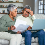 Shot of a senior couple looking stressed while using a laptop and going through paperwork on the sofa