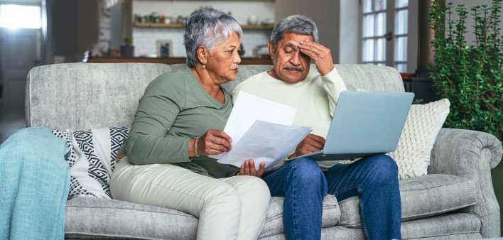 Shot of a senior couple looking stressed while using a laptop and going through paperwork on the sofa