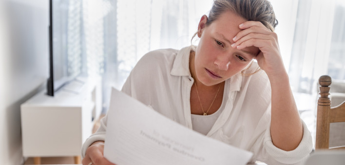 Woman looking worried holding paperwork at home. She is reading a financial bill or a letter with bad news. She looks very stressed and upset.