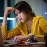 Young woman with laptop computer for homework. Tired hispanic girl and college education. Female student studying and using pc at home getting headache