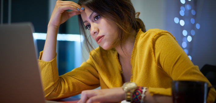 Young woman with laptop computer for homework. Tired hispanic girl and college education. Female student studying and using pc at home getting headache