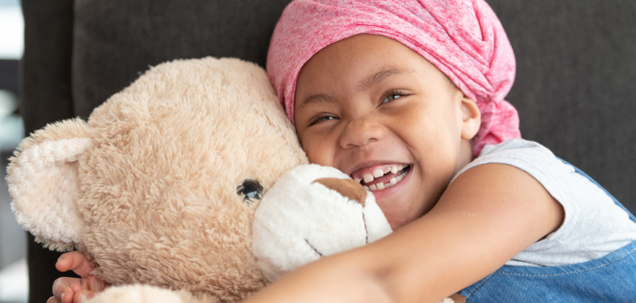 Happy girl with cancer hugs large teddy bear
