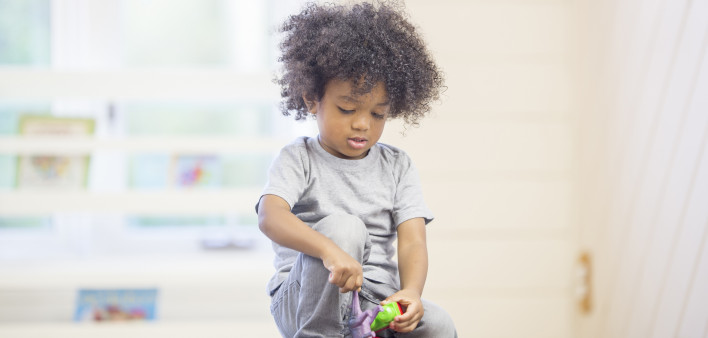 A cute little boy is sitting on the floor playing with building blocks at preschool.