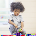 A cute little boy is sitting on the floor playing with building blocks at preschool.