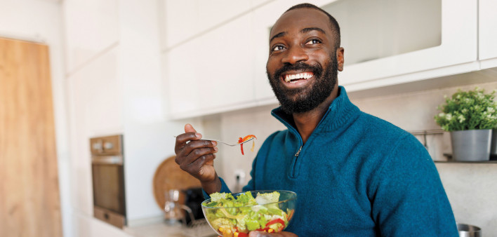 young black man smiling eating a salad