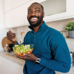 young black man smiling eating a salad